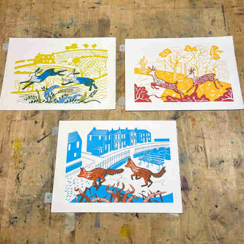 Three screenprints of animals. Top left are two hares in dark green and blue leaping over wheat with a yellow background of fields. Top right are leaping stags in red and orange with a background of yellow trees. At the bottom are leaping foxes in orange and brown leaping over grasses with houses in blue in the background.