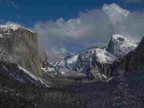 Snow Kissed Valley

This is an image of Yosemite Valley captured from the Tunnel View 
overlook. 
The valley and surrounding areas are blanketed in snow as a storm is clearing. Broken clouds can be seen at the eastern end of the park.
On the left side of the image is El Capitan, a 3,000 foot monolith that seems to guard the valley. On the right side of the image is Bridalveil Falls. Above the falls are the snow covered Three Brothers. Further back in the image is Half Dome.

