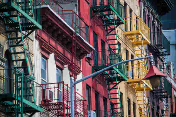 Colorful facades of urban buildings with external fire escapes, featuring a red, white, and yellow building side by side.