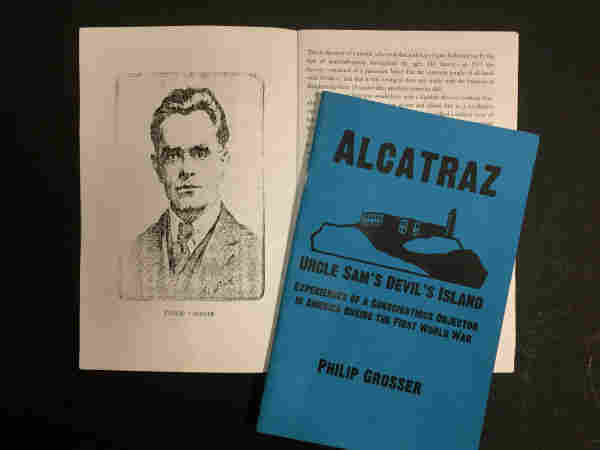 Cover of Grosser's pamphlet, "Alactraz, Uncle Sam's Devil's Island," with blue cover and sketch of the prison building on Alcatraz island. The pamphlet is laying over a page in Grosser's biography, with a sketch of Grosser, looking straight ahead, clean shaven, in a suit and tie.