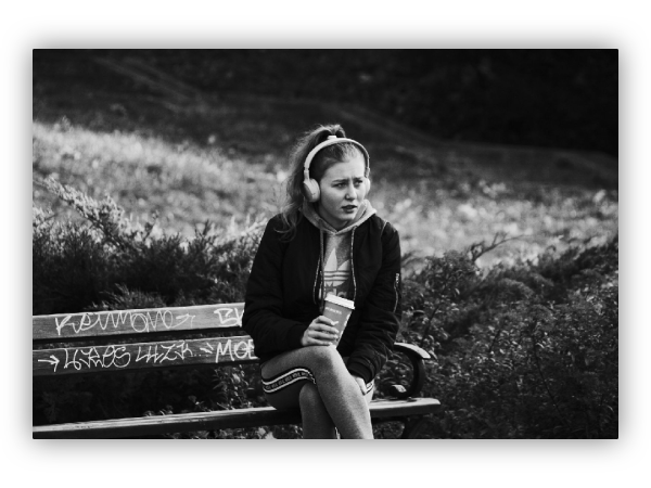 Girl with headphones and a mug of coffee sitting on a bench.