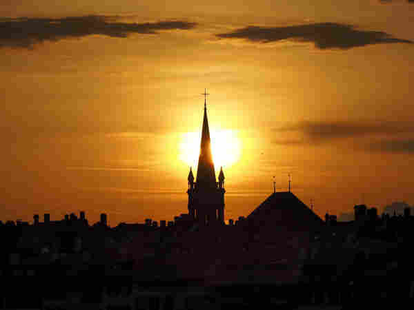 Sunset behind a church steeple in the old town of Bern with a silhouette of rooftops in the foreground.