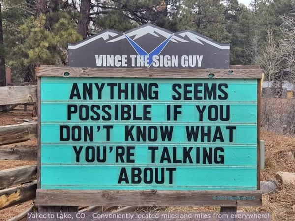 Still image. Wood-framed church sign, teal background, black text. Reads:
ANYTHING SEEMS
POSSIBLE IF YOU
DON'T KNOW WHAT
YOU'RE TALKING 
ABOUT