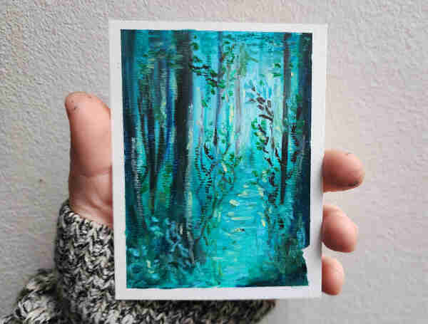 My hand holding up a little blue-green oil pastel forest scene