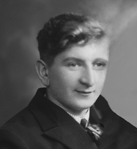 Vintage black-and-white portrait of a young man with wavy hair, wearing a formal suit and tie.