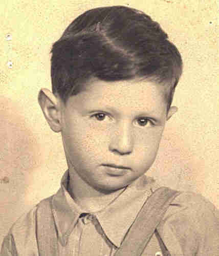 Portrait photograph of a young boy's face. He has dark short hair. He is dressed in a shirt buttoned up to the neck. You can see that he is wearing braces. His head is tilted a little to the right and he is looking straight into the lens.