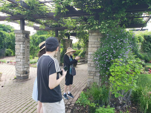 Young man, his young wife (my daughter) looking at older woman in straw hat taking photo of a flowering vine.