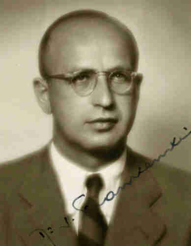 An ID sepia photo of a man in a jacket, shirt and tie. He is wearing glasses. He has very short hair and exposed forehead.