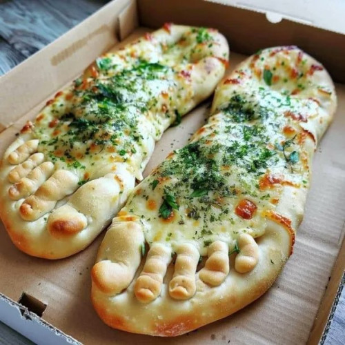 Still image. Square cardboard pizza box with two oblong pieces of baked bread, cheese and herbs on top, and they have toes. They're bread feet. 