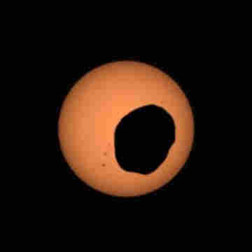 Photo of a large orange circle (the sun) about 30% covered by a mishapen lumpy black blob
