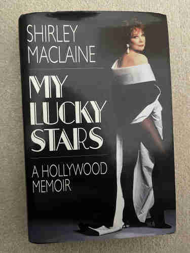 Cover of My Lucky Stars, A Hollywood Memoir - Shirley MacLaine. Photo is the author, wearing a sort of silk shawl thingy, and her legs go on forever.