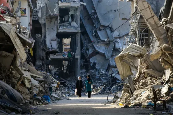 Palestinian women make their way past destroyed buildings in Khan Younis [Eyad Baba/AFP]