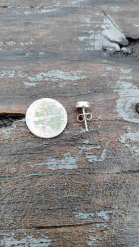 An earring lies on a wood surface beside a dime, for size reference