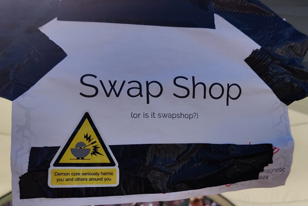 Swap shop sign with a hazard sticker that says "Demon core seriously harms you and others around you".