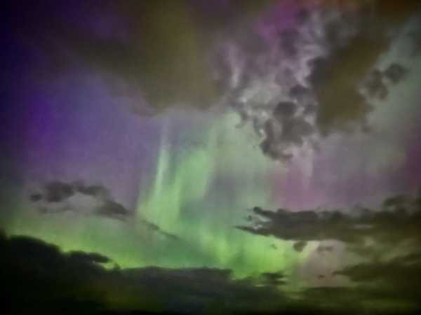 Swirls of green aurora with some clouds and a purple sky