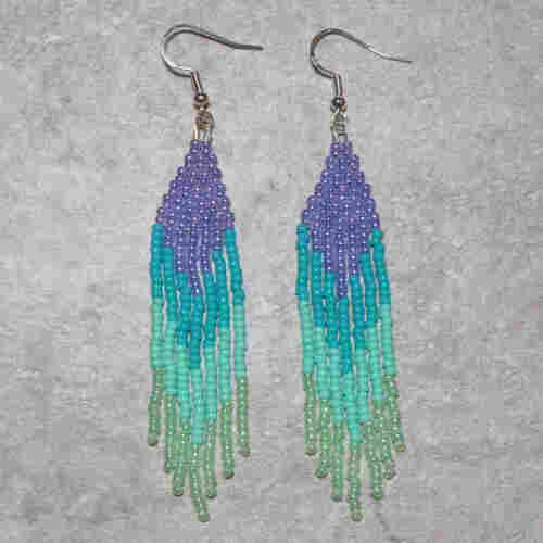 Purple, blue, and sea foam green Native beaded fringe earrings on a stone background