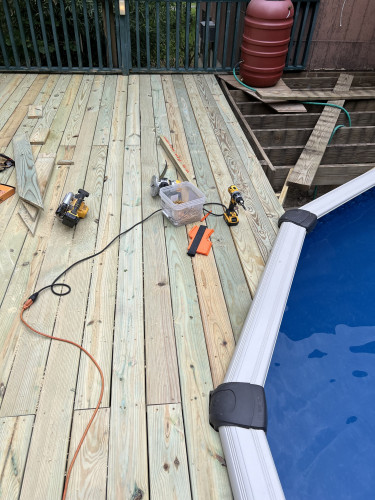 Picture of a partially finished deck around a pool.  There are various tools in view including a cordless drill, router, and circular saw.  A tub of screws is also visible.