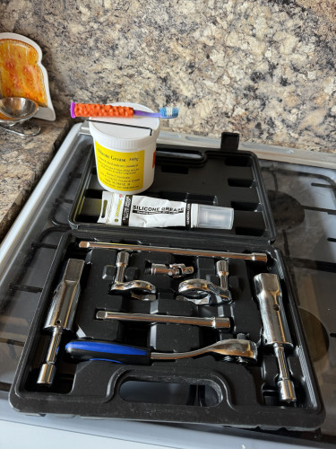 Picture a multi-part ratchet tap spanner set, with 2 tap box spanners & various other accessories. There is also a 2.5mm Allen key , an orange & purple child’s toothbrush , a tub of potable silicone grease & a tube of general purpose silicone grease . Also a cottonwool ear bud
