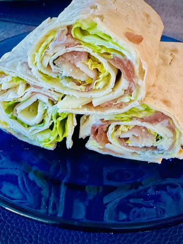 Close view of 3 rolled sandwiches made of lavash bread and filled with ham, cheese and lettuce. On a cobalt blue glass plate. 