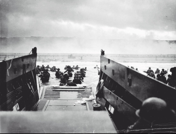 Black and white photo from the operation overlord, also called dday.

View from a landing boat with open tailboard (is this the right word here) at the shore. Soldiers wading through the water towards the beach.