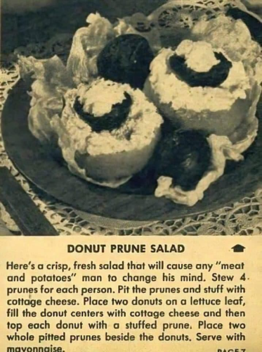 A black and white photo of a plate with some lettuce, two donuts stuffed with things and some prunes for decoration. Text reads
Donut Prune Salad. Here's a crisp, fresh salad that will cause any "meat and potatoes" man to change his mind. Stew 4 prunes for each person. Pit the prunes and stuff with cottage cheese. Place two donuts on a lettuce leaf, fill the donut centres with cottage cheese and then top each donut with a stuffed prune. Place two whole pitted prunes beside the donuts. Serve with mayonnaise. 