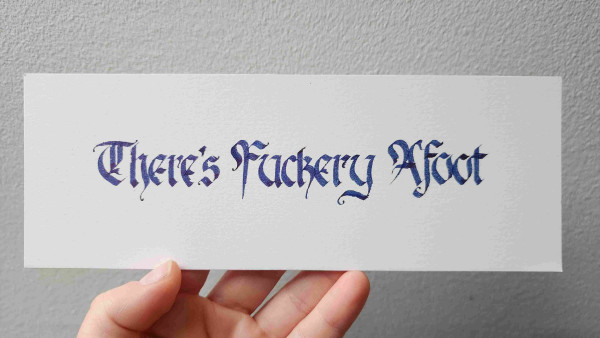 'There's Fuckery Afoot' calligraphied in blackletter script in dark blue sparkly ink