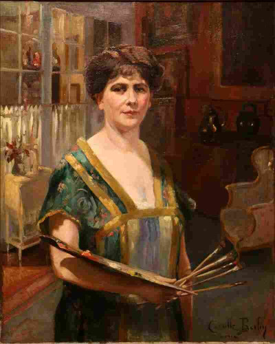 Camille Berlin in self portrait 1914, wearing a darke green and gold dress, holding palette and brushes, dark brown hair piled on top of head, looking directly at viewer. Domestic looking background of window on left and armchair on right