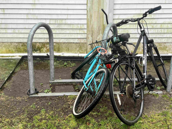 A bike rack with two bikes attached sitting in a big muddy puddle of rainwater next to Town Hall in Provincetown.