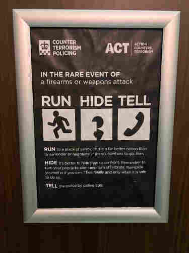 A poster pinned to the door of a public restroom, giving instructions (run, hide, tell) for what to do if you find yourself caught up in a firearms or weapon attack. 