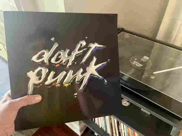 Photo of a hand holding Daft Punks “Discovery” LP in front of a turntable