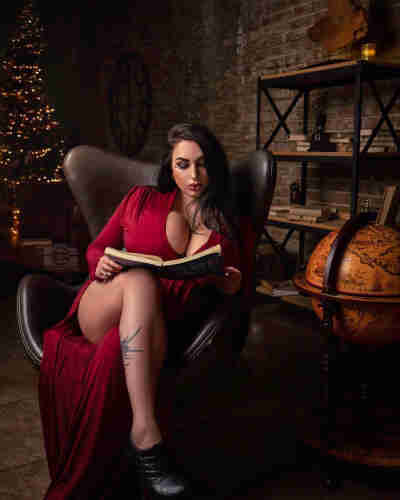 Generated description:
A stunning woman with long, dark hair sits gracefully in a leather armchair, clad in a striking red dress that accentuates her elegant figure. Behind her, a towering Christmas tree adorned with twinkling lights and shiny baubles adds a festive touch to the scene. The woman's posture exudes confidence and poise as she gazes intently at the book in her hands, her fingers delicately tracing the pages. The room is dimly lit, with a soft glow casting a warm light on the woman's features. In the background, a shelf lined with books and a globe can be seen, adding a scholarly vibe to the image. The image captures a peaceful moment, where the woman is lost in her own world, surrounded by the comforting familiarity of her home. Her serene expression and the cozy setting make us feel like we are peeking into a private moment, adding a sense of intimacy to the photograph.
