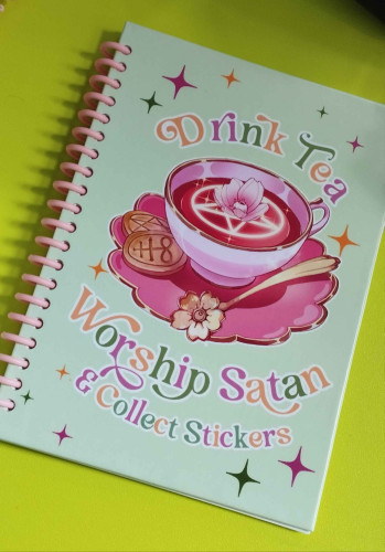 Spiral bound stickerbook showing a tea cup with a pentagram and flower with eyeball floating on the tea. Text says "drink tea, worship satan & collect stickers".