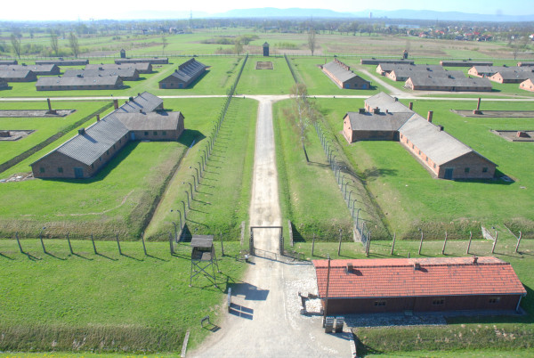 Aerial view of the former Auschwitz II-Birkenau camp showing rows of barracks, fencing, and the expansive layout of the grounds under clear skies.