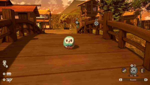 A shiny rowlet standing on a bridge in Pokémon Legends: Arceus. His feathers are teal with a blue bow tie, rather than brown feathers and a green bow tie in his non-shiny form