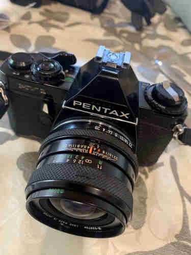 Black Asahi Pentax MV1 film camera with lens on a patterned surface.
