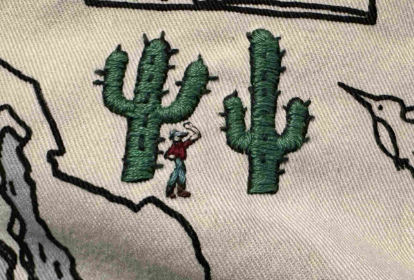 Two smallish embroidered saguaro cactus with a tiny embroidered person. 
