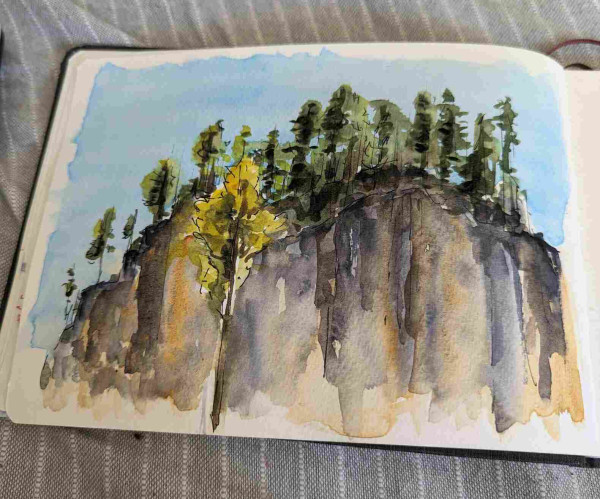 Watercolor sketch of a high rocky cliff with pine trees lining the edge, reaching into the blue sky. One tree in front of the cliff is lit by the sun 