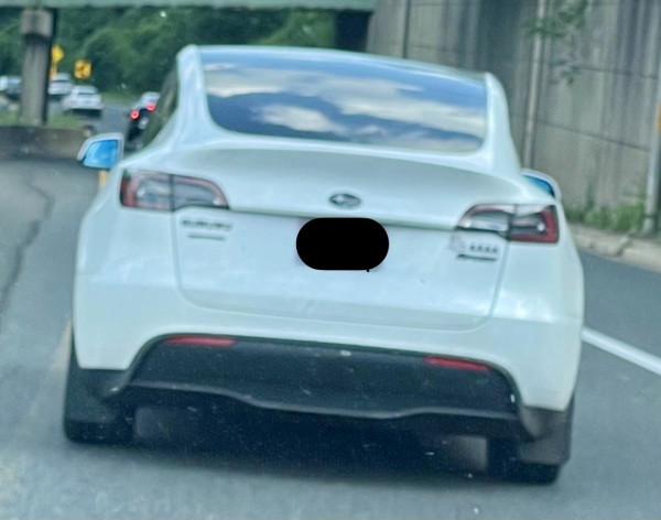 A white Tesla model Y sporting a Subaru badge and other Subaru-related decals… no Tesla banding visible.