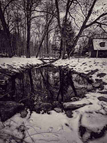 A monochromatic image  of a pool of standing water lying amongst snowy grounds