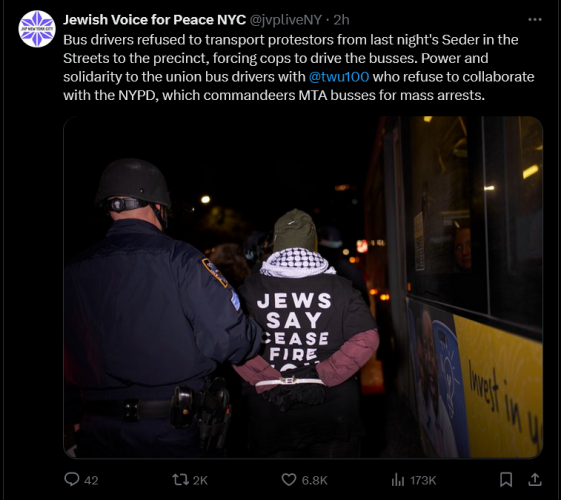 Picture of an NYPD officer leading a Jewish activist to a bus.  The activist is wearing a keffiyeh and a tshirt reading JEWS SAY CEASEFIRE NOW
Jewish voice for Peace NYC accompanying text reads:
Bus drivers refused to transport protesters from last night's Seder in the Streets to the precinct, forcing cops to drive the buses.  Power and solidarity to the union bus drivers with @twu100 who refuse to collaborate with the NYPD, which commandeers MTA buses for mass arrests.