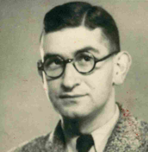 An ID-style photo of the face and shoulders of a man in round-framed glasses. He is wearing a jacket, shirt and tie. He has short dark hair.