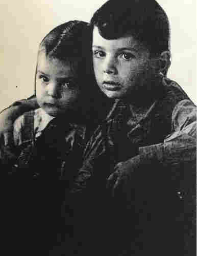 A photo of a young boy with his sister. The girl hugs her brother and he puts his arm around her.