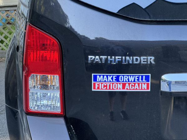 A black SUV has a blue and red bumper sticker, emulating you-know-who's, but this one says:

"Make Orwell Fiction Again"