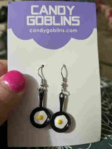 A set of earrings in the shape of frying pans. Each has an egg, sunny side up, in it. 