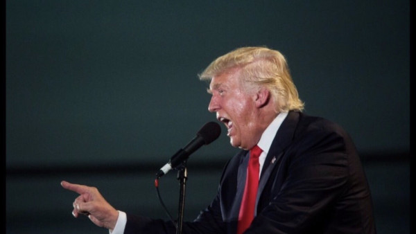 Donald J. Trump, from a side view, ranting from a podium while pointing out at the audience. He’s sweating profusely.
