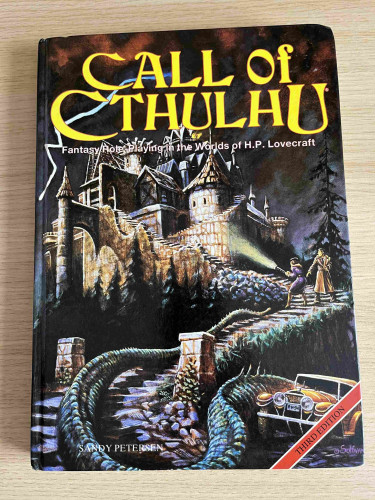 The Games Workshop hardback edition (available 3rd edition) of Call of Cthulhu. The cover depicts a Victorian house with winding steps leading up to the front door and a yellow car at the bottom. Halfway ip the steps are a couple of investigators shining a torch at the house. What they don’t see, but we do, is the tentacle slithering up the stairs behind them. 