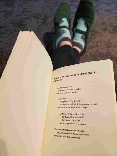 Sitting on the floor reading the poetry collection Lossless by Matthew Tierney, open to the poem "Stranded on the Jungle Gym After Morning Bell in Kindergarten". My feet in green mary jane shoes and blue and gray patterned socks are visible in the background.
The poem includes:

"Tossed by an east wind
   atop marrowless metal shafts:
viaducts of alternate choices:

   I stand as I."