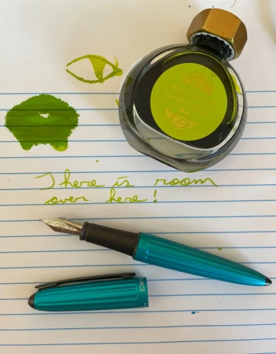 Ferris Wheel Frivolous Lime ink bottle laying beside a small spill of ink on a note pad.  Blue Diplomat Aero fountain pen lays uncapped below some cursive or script writing :

There is room over here!

