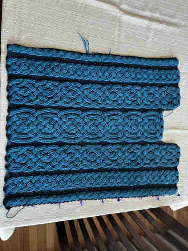 Mostly rectangular crochet fabric with a notch at one side for the neckline. It has turquoise cables in several patterns against a dark blue-black background.