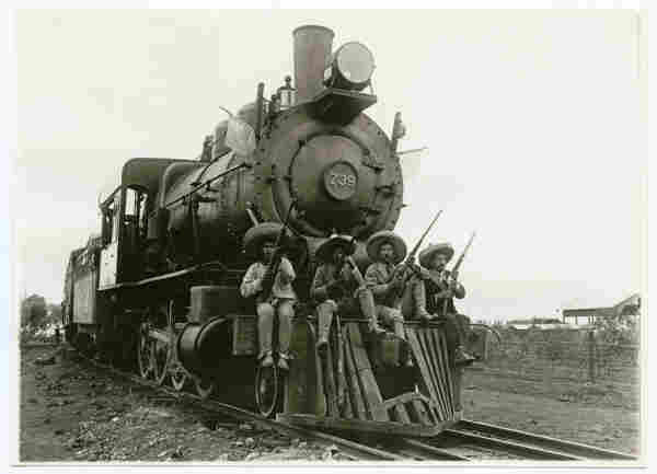 Zapatistas in Cuernavaca, 1911, riding on the cattle catcher of a locomotive, with sombreros and rifles. Hugo Brehme, photographer. By SMU Central University Libraries - [Zapatistas and Nacional de Mexico, No. 739], No restrictions, https://commons.wikimedia.org/w/index.php?curid=44017484